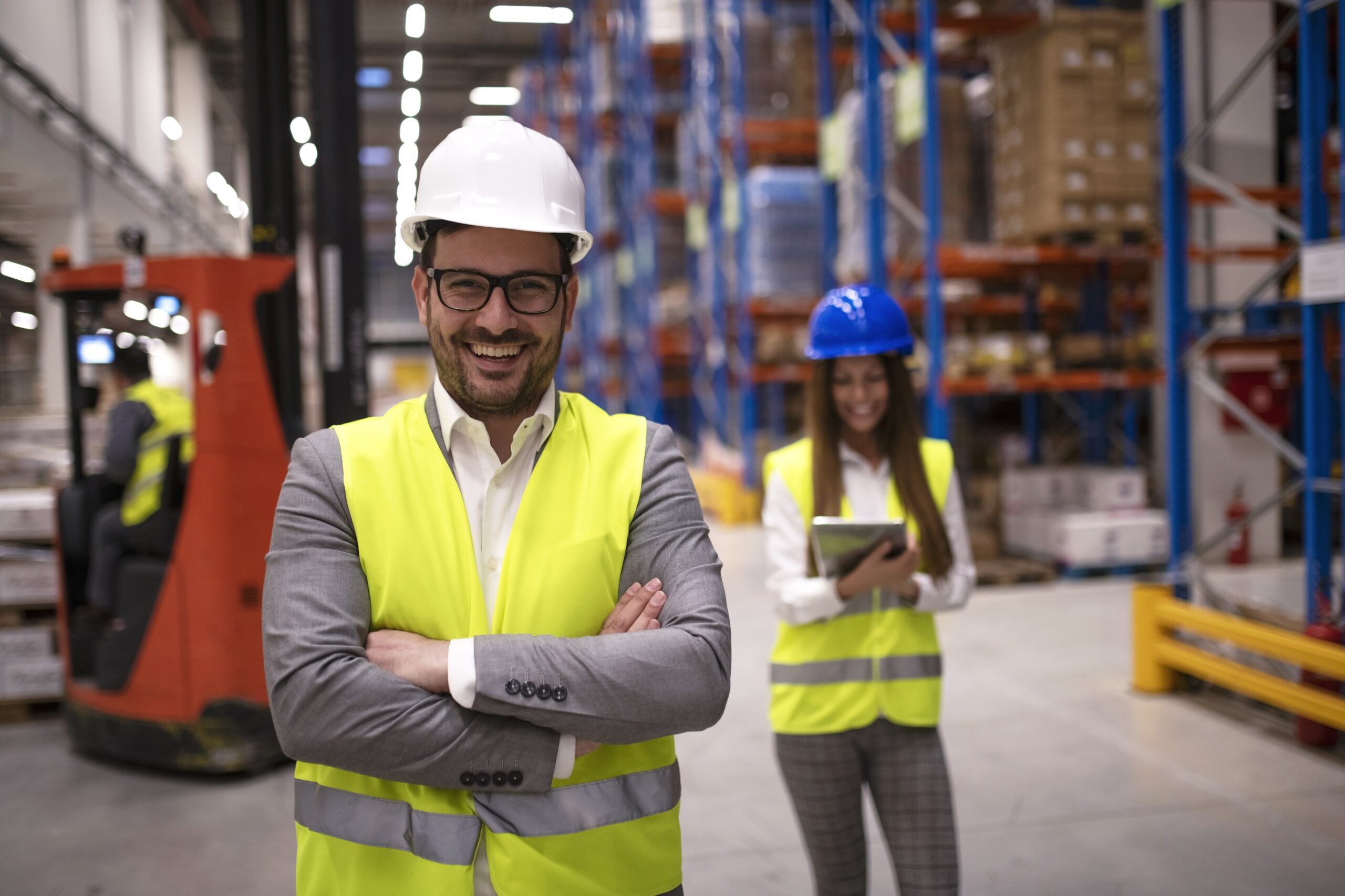 Portrait of successful warehouse worker or supervisor with crossed arms standing in large storage distribution area.